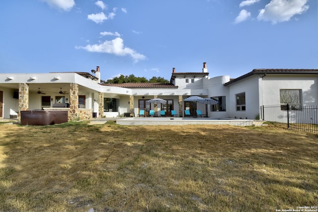 rear view of property featuring ceiling fan, fence, stucco siding, a patio area, and a hot tub