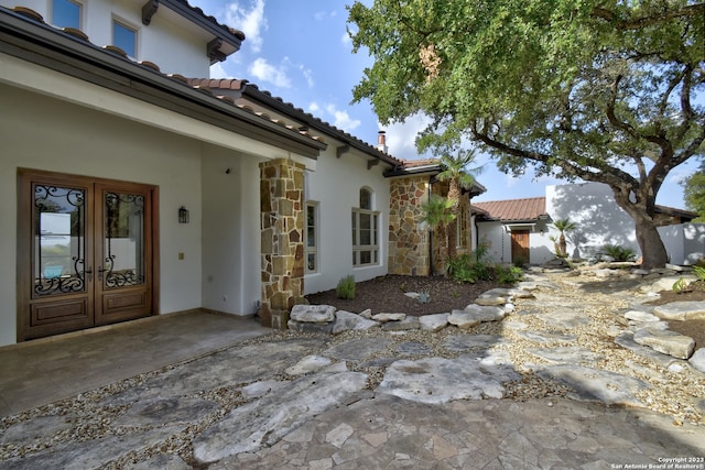 view of side of property with stone siding, french doors, a tiled roof, and stucco siding