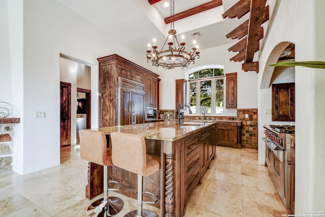 kitchen with an island with sink, high quality appliances, decorative light fixtures, light stone countertops, and a sink