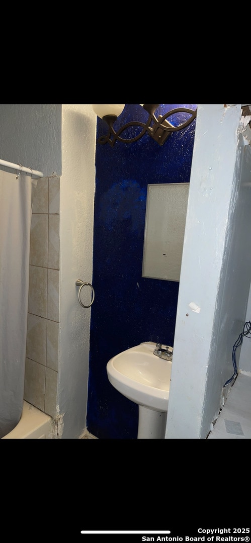 full bathroom featuring a textured wall, curtained shower, and a sink