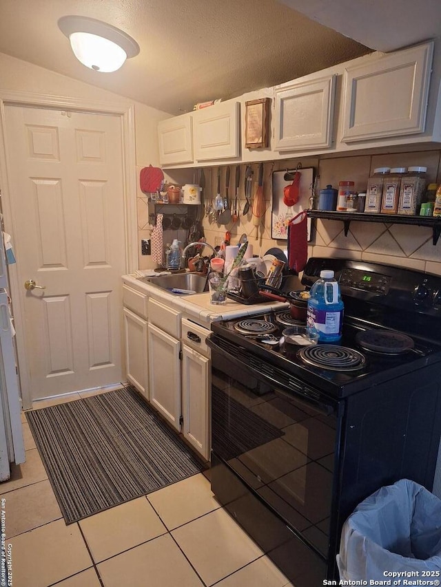 kitchen featuring black electric range, light tile patterned floors, light countertops, white cabinets, and a sink