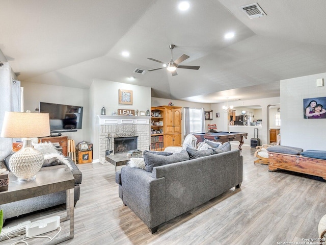 living area featuring a brick fireplace, visible vents, vaulted ceiling, and light wood finished floors