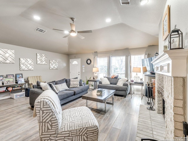 living room featuring visible vents, a ceiling fan, light wood-style flooring, vaulted ceiling, and a fireplace