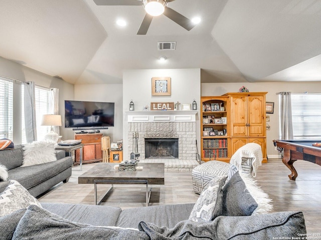 living room with vaulted ceiling, a wealth of natural light, a brick fireplace, and visible vents