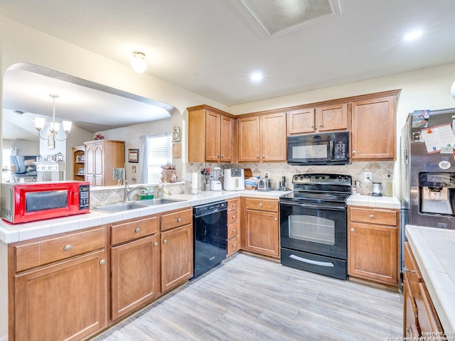 kitchen with a peninsula, a sink, light wood-type flooring, decorative backsplash, and black appliances