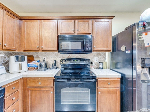 kitchen with tile countertops, black appliances, and backsplash