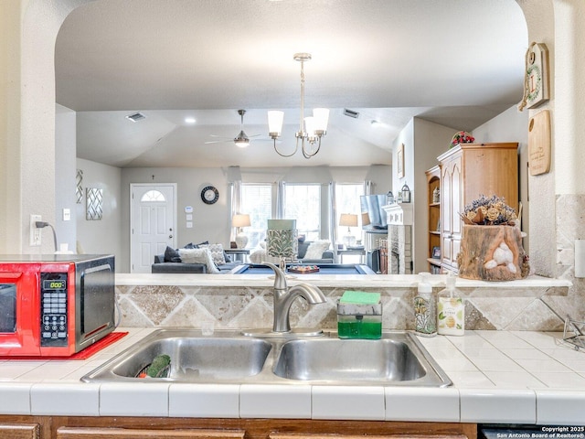 kitchen with a notable chandelier, a sink, open floor plan, vaulted ceiling, and tile counters