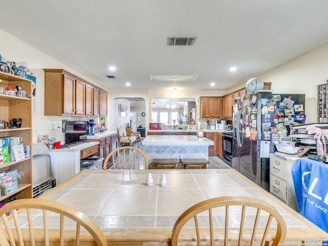 kitchen featuring arched walkways, tile countertops, visible vents, black electric range, and brown cabinetry