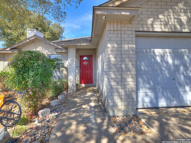 view of exterior entry with a garage and brick siding