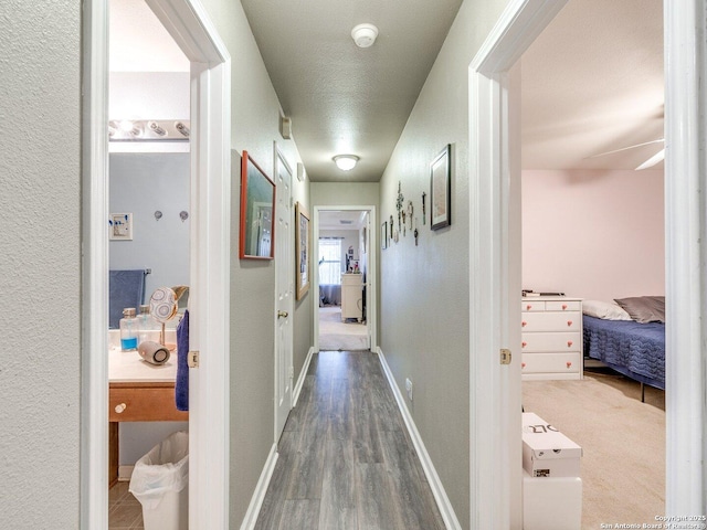 hallway with a textured wall, baseboards, and wood finished floors