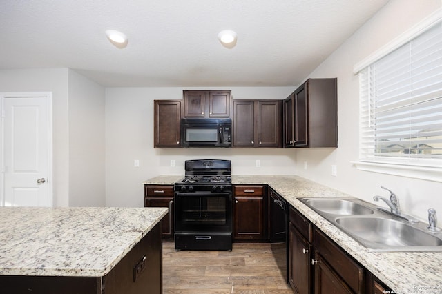 kitchen with a textured ceiling, dark brown cabinetry, a sink, black appliances, and light wood finished floors