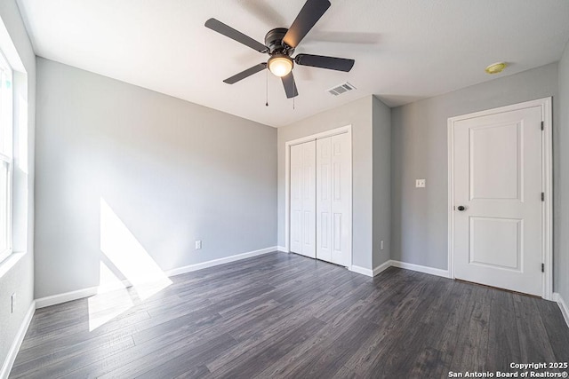 unfurnished bedroom featuring dark wood-style flooring, a closet, visible vents, and baseboards