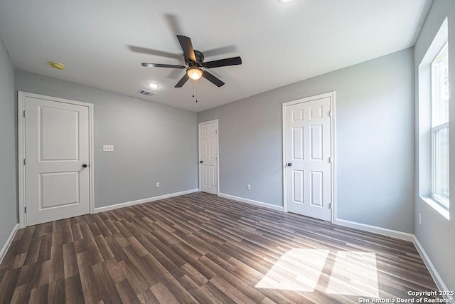 unfurnished bedroom with visible vents, dark wood finished floors, baseboards, and multiple windows