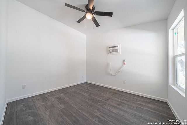 unfurnished room with an AC wall unit, dark wood finished floors, a ceiling fan, and baseboards