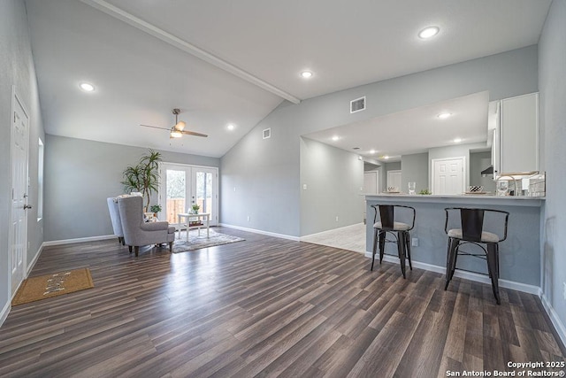 interior space with french doors, vaulted ceiling with beams, dark wood-type flooring, white cabinets, and a kitchen breakfast bar