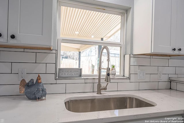 kitchen with light stone countertops, backsplash, and a sink