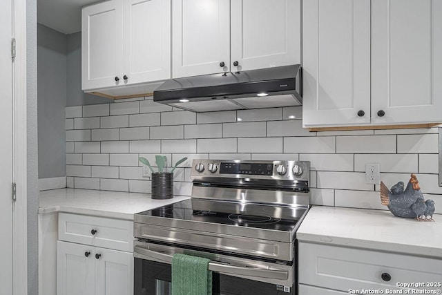 kitchen with tasteful backsplash, white cabinets, under cabinet range hood, and stainless steel electric range