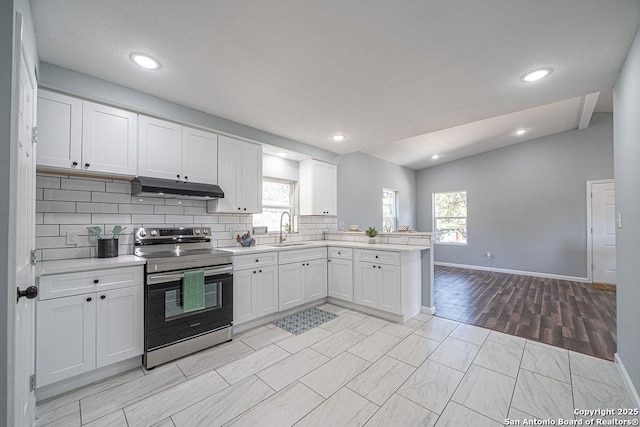 kitchen featuring electric stove, a peninsula, light countertops, under cabinet range hood, and a sink