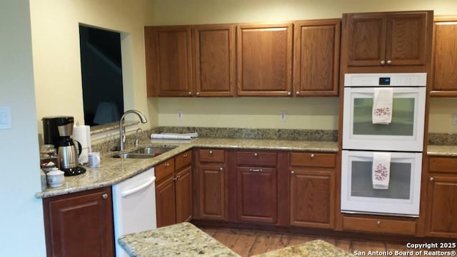 kitchen with light stone counters, white appliances, brown cabinets, and a sink