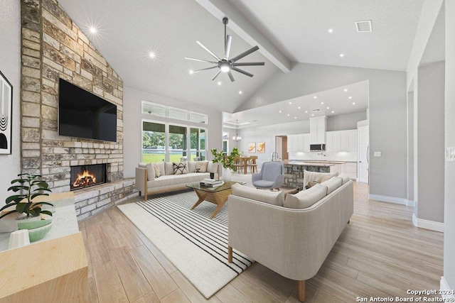 living area featuring high vaulted ceiling, light wood-type flooring, visible vents, and a fireplace