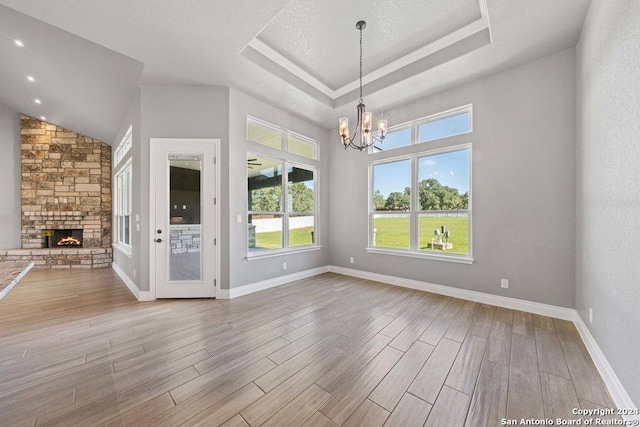 unfurnished dining area with a fireplace, a raised ceiling, an inviting chandelier, wood finished floors, and baseboards