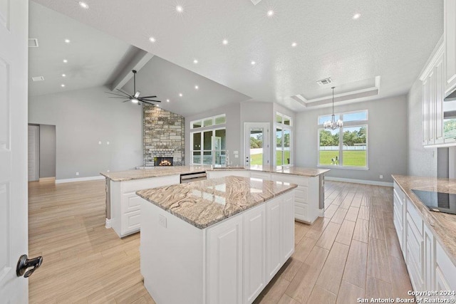 kitchen with a stone fireplace, ceiling fan with notable chandelier, a spacious island, open floor plan, and light wood-type flooring