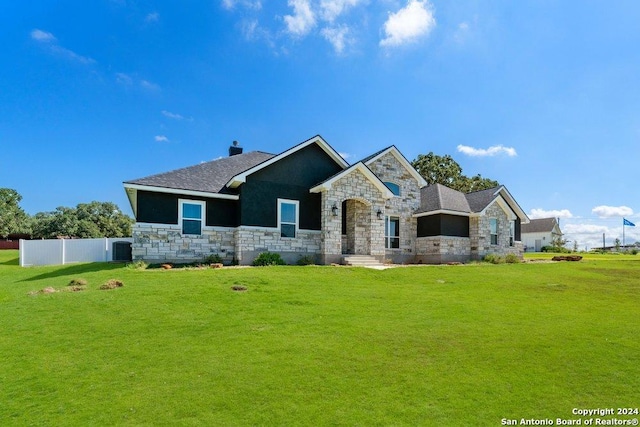 view of front of house with central air condition unit, stone siding, fence, and a front lawn