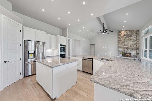 kitchen featuring a fireplace, stainless steel appliances, a spacious island, light wood-style floors, and a sink