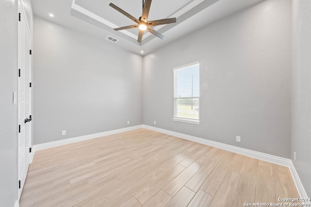 empty room with light wood-style flooring, a ceiling fan, visible vents, baseboards, and a tray ceiling