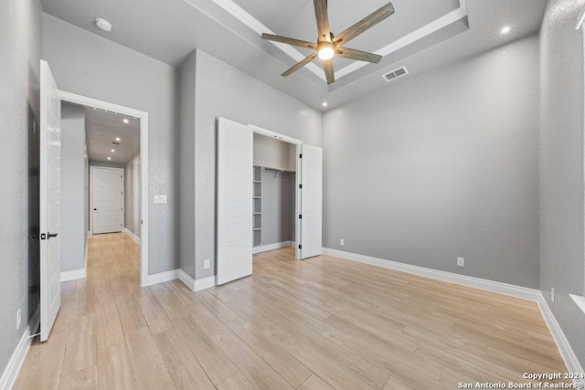 unfurnished bedroom featuring visible vents, baseboards, light wood finished floors, a tray ceiling, and a walk in closet