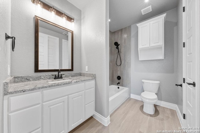 full bath featuring toilet, wood finished floors, vanity, baseboards, and washtub / shower combination