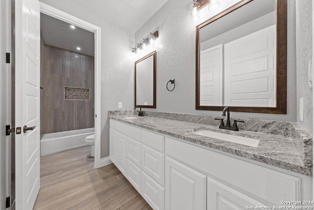 full bathroom featuring double vanity, wood finished floors, a sink, and toilet