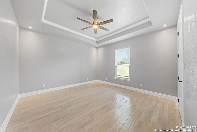 spare room with a raised ceiling, ceiling fan, a textured ceiling, light wood-type flooring, and baseboards