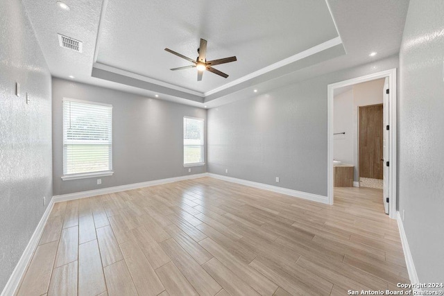 spare room with light wood-type flooring, a raised ceiling, and visible vents