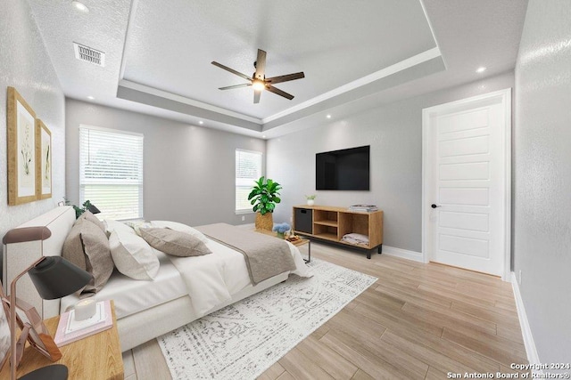 bedroom with baseboards, a raised ceiling, visible vents, and light wood-style floors