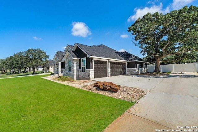 view of side of home with an attached garage, fence, stone siding, a yard, and driveway