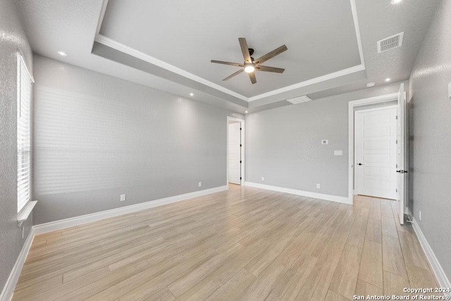 spare room featuring light wood-style floors, a tray ceiling, visible vents, and baseboards