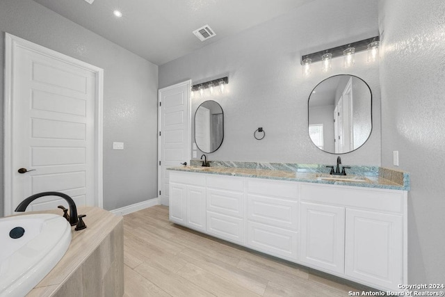 bathroom featuring wood finished floors, visible vents, a sink, and double vanity