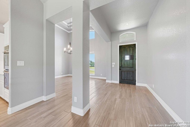 entryway with light wood-type flooring, a textured ceiling, baseboards, and an inviting chandelier