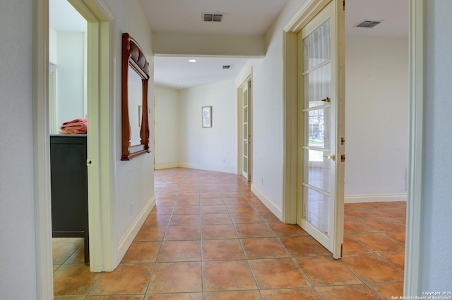 hallway with tile patterned flooring, visible vents, and baseboards