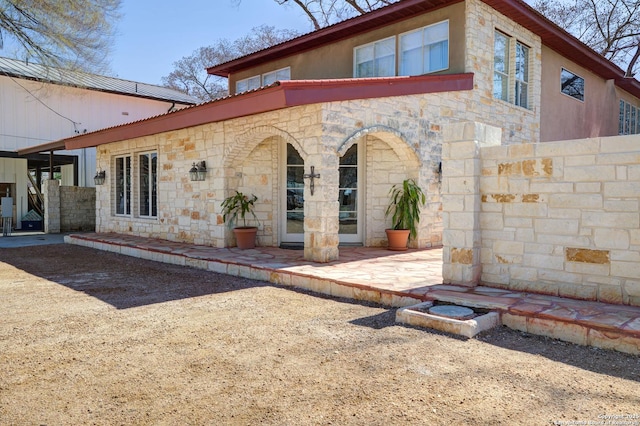 back of property with a patio area, stone siding, metal roof, and fence