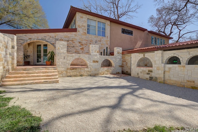 back of property featuring french doors, stone siding, driveway, and stucco siding