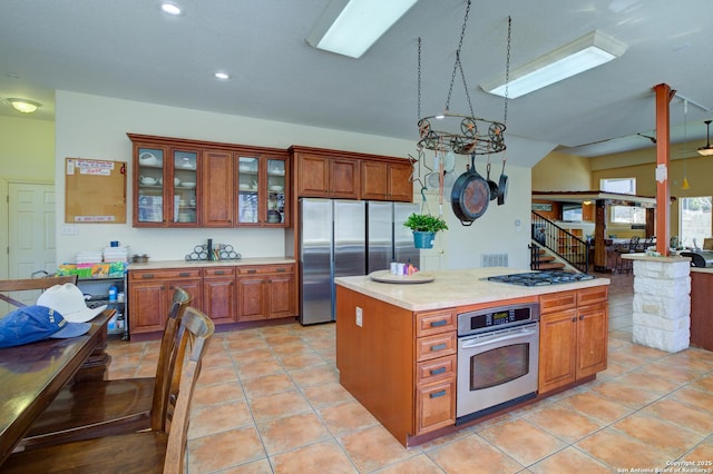 kitchen with brown cabinetry, glass insert cabinets, stainless steel appliances, and light countertops