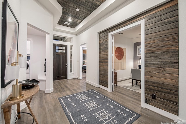 entrance foyer with wood finished floors, visible vents, baseboards, washer / clothes dryer, and a raised ceiling