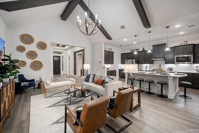 living area with beam ceiling, light wood-type flooring, visible vents, and an inviting chandelier