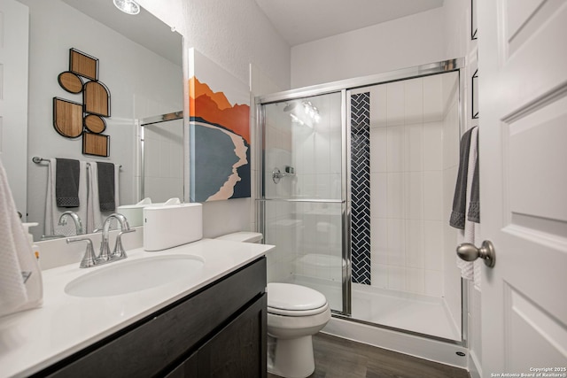 bathroom with toilet, a shower stall, wood finished floors, and vanity