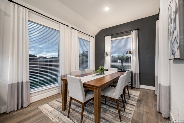 dining area featuring a textured wall, vaulted ceiling, baseboards, and wood finished floors