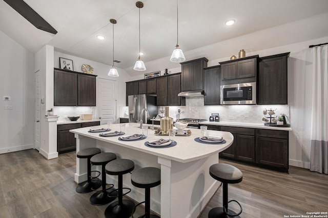 kitchen featuring a breakfast bar, light countertops, decorative backsplash, appliances with stainless steel finishes, and under cabinet range hood