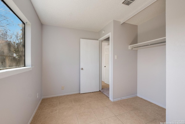 unfurnished bedroom with a textured ceiling, light tile patterned flooring, visible vents, baseboards, and a closet