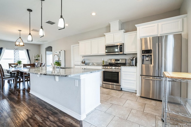 kitchen featuring light stone counters, arched walkways, a breakfast bar, stainless steel appliances, and white cabinets